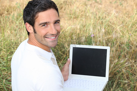 带着笔记本电脑坐在草地上微笑的男人