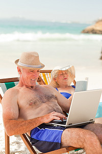 男人在笔记本电脑上工作，而他的妻子在沙滩上看书