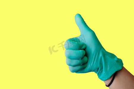 戴着蓝色乳胶手套的女性手在浅黄色背景上竖起大拇指，就像孤立的手势一样。