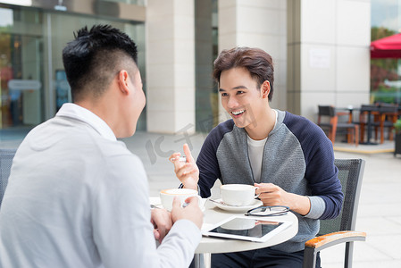 朋友讨论摄影照片_两个亚洲男人坐在咖啡馆里讨论