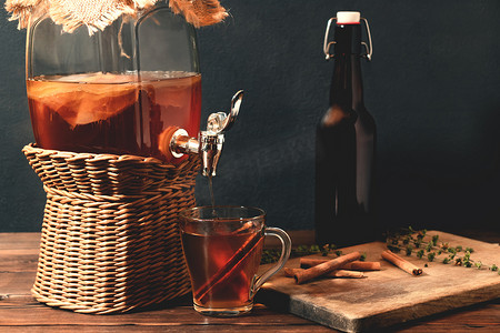 新鲜自制康普茶发酵茶饮料，装在带水龙头的罐子里，装在黑色背景的杯子和瓶子里