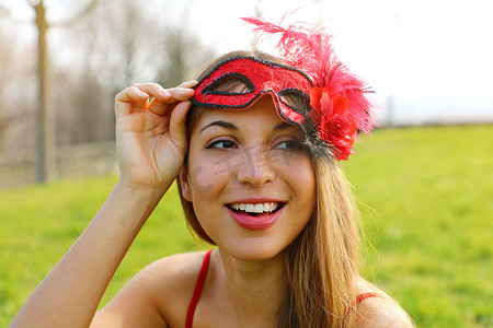 年轻女子在户外狂欢节派对后在草地上醒来后摘下狂欢节面具的特写，向侧面看