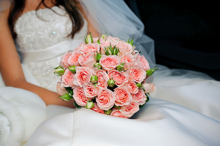 穿着白色礼服的新娘手捧一束精美的玫瑰花