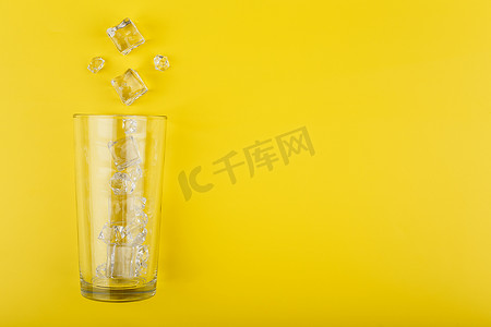 黄色背景简单摄影照片_平躺着空的透明玻璃，黄色背景上有溢出的冰块，有复制空间