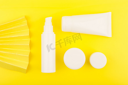 创意瓶中摄影照片_黄色背景上用波纹装饰的白色无品牌管中护肤化妆品的顶部视图