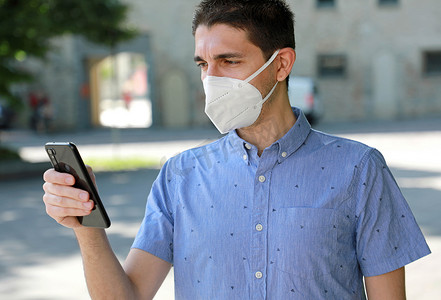 COVID-19 移动应用程序年轻人戴着 KN95 FFP2 面具在城市街道使用智能手机应用程序帮助接触者追踪和自我诊断以应对 2019 年冠状病毒大流行