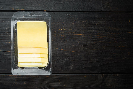 切片美味的伊丹奶酪，塑料包装，黑色木桌背景，顶视图平躺，带文本复制空间