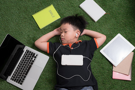 小男孩躺在草地上，戴着耳机听音乐
