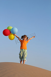 拿着气球站在沙丘上的快乐小女孩