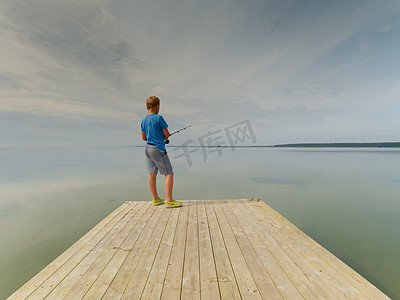 沙滩鞋摄影照片_金发小男孩正在木鼹鼠的尽头钓鱼。