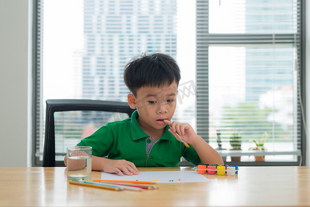 学习创意背景摄影照片_孩子们在学习桌上思考。孩子拿着笔和笔记本与思考的面部动作。男孩在学习桌上做作业与思考行为。