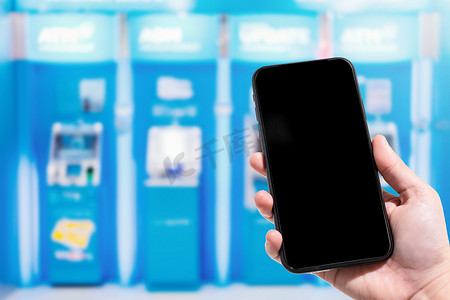 在百货商店的 ATM 机蓝色模糊中，女性使用手持智能手机模糊图像触摸抽象模糊。