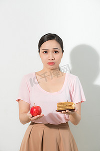 拿着苹果摄影照片_女孩一只手拿着苹果，另一只手拿着蛋糕。