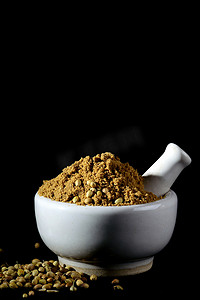 香菜粉和种子与砂浆和杵在黑色背景上。