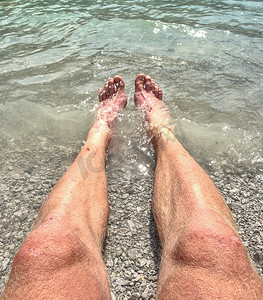 腿和脚踩在有湖水或海水的海滩石头上。