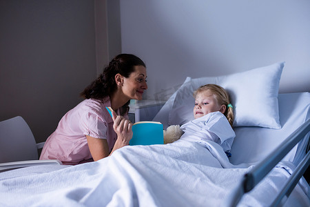 在医院病床上看书的女孩和她的母亲