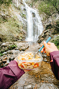 一位女性徒步旅行者在瀑布前吃饭的视角镜头