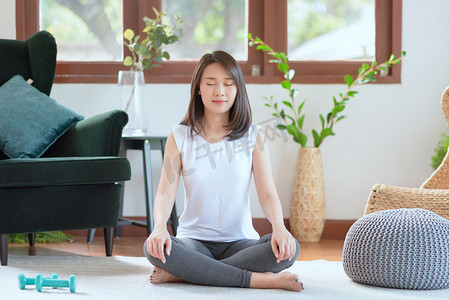 饮食健身摄影照片_美丽的亚洲女性在家练习瑜伽时保持冷静和冥想，以追求健康的潮流生活方式