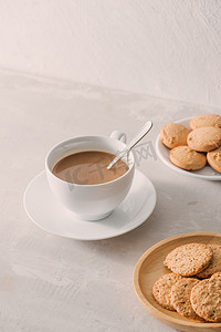 早上喝牛奶摄影照片_一杯加牛奶的咖啡或卡布奇诺配浅色石头背景上的饼干。