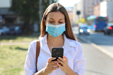 COVID-19 大流行冠状病毒年轻女性戴着外科口罩在城市街道使用智能手机应用程序帮助追踪接触者以应对 2019-20 冠状病毒大流行