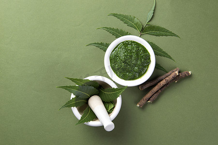 药用尼姆叶在砂浆和杵中，绿色背景上有糊状物和树枝