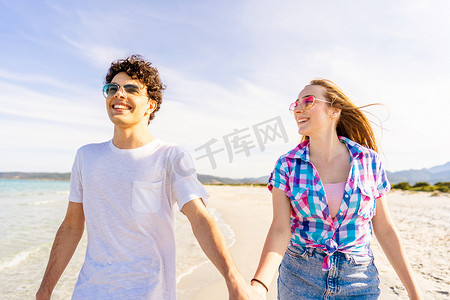 无忧无虑的青年概念：年轻非常快乐的 z 世代真正的夫妇牵着手在夏天带着太阳镜温柔地走在热带海滩的海边。
