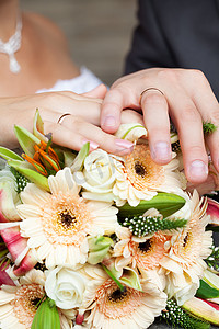 新娘和新郎的手放在新娘捧花上