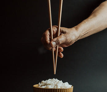 极简主义的老手在一碗米饭上抓着日本筷子，概念是在黑色背景下用电影色调拍摄的