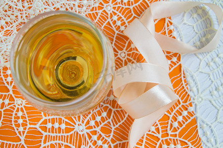 将白葡萄酒平放在玻璃杯中，米色蕾丝和装饰丝带，橙色背景，顶视图。