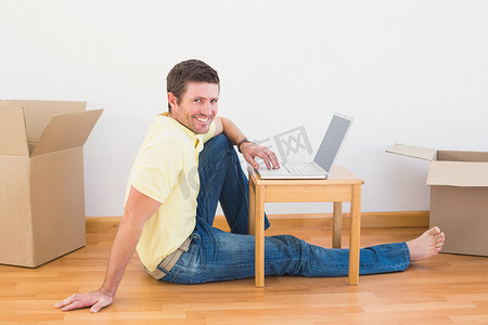 随便摄影照片_随便的男人坐在地板上，在家里的咖啡桌上使用笔记本电脑