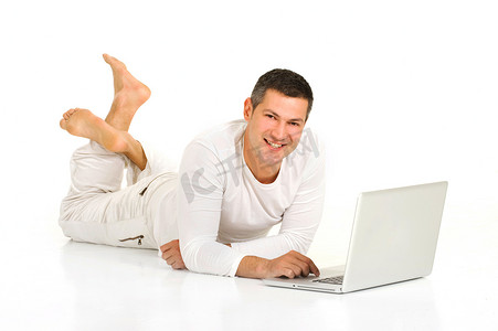 光脚躺摄影照片_穿着白色衣服的男人躺在地板上，拿着笔记本电脑