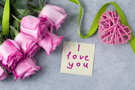 一束粉红玫瑰、一颗心和一张纸条，桌上写着我爱你 — 爱与关怀的概念