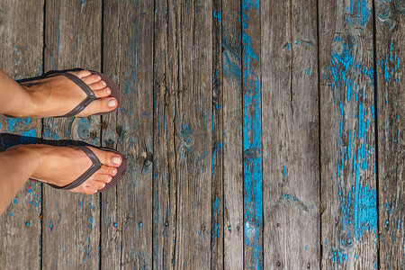 沙滩拖鞋摄影照片_顶视图，女性腿的照片在木 o 上的沙滩拖鞋