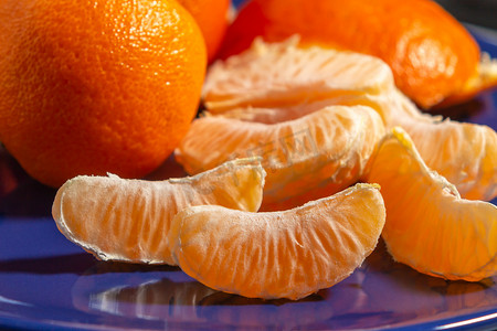 蓝盘上几个完整的和去皮的成熟橘子