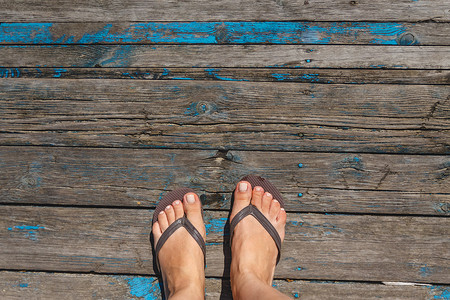 沙滩拖鞋摄影照片_顶视图，女性腿的照片在木 o 上的沙滩拖鞋