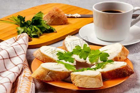 新鲜制作的三明治，盘子上放着奶油奶酪和欧芹，切木板和一杯咖啡 — 早餐概念