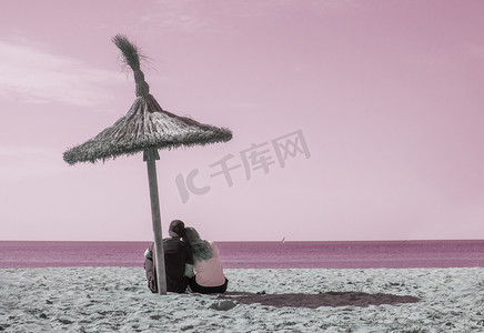 年轻自然和休闲的运动夫妇坐在遮阳伞下的海滩上