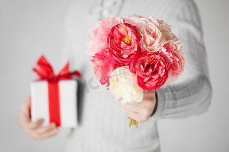 红色牡丹摄影照片_拿着一束鲜花和礼品盒的男人