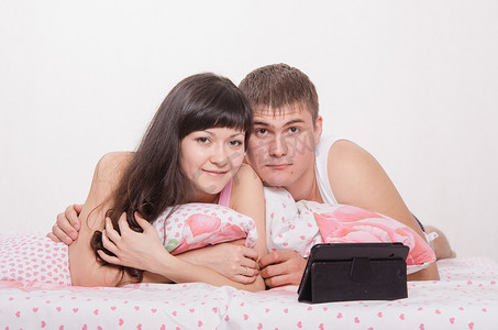 电脑电影摄影照片_躺在床上用平板电脑的年轻夫妇