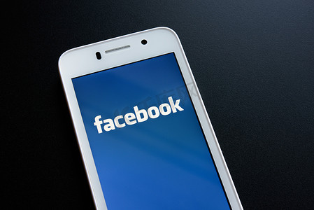 脸谱网摄影照片_ZAPORIZHZHYA，乌克兰-2014 年 11 月 7 日： 白色智能手机与 Facebook 社交网络登录屏幕在黑桌上。