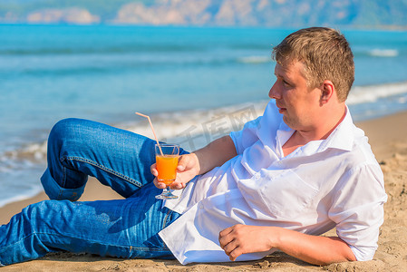 光脚躺摄影照片_一个男人穿着衣服躺在沙滩上喝鸡尾酒