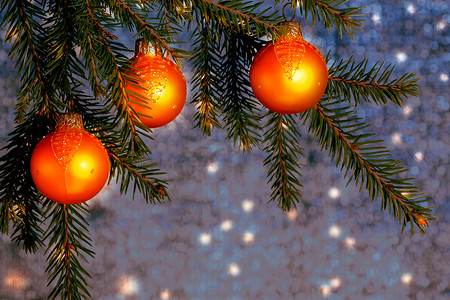 银蓝摄影照片_闪亮的蓝银背景上云杉枝条上的橙色圣诞饰品。