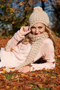 围巾女摄影照片_秋天带着帽子和围巾在户外微笑的年轻女人