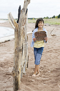 日志标志摄影照片_海滩上的小女孩举着空白的木牌