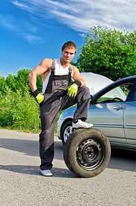 英俊的机械师站在路上的轮胎上