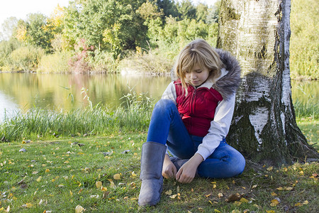 湖边秋季公园树下坐着的小女孩