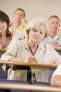 坐在成人教室里的女性在背景中与学生一起做笔记（有选择的焦点）