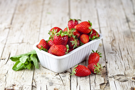 白草莓摄影照片_白碗里的新鲜红草莓和质朴的 w 上的薄荷叶