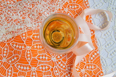 丝带邀请函摄影照片_将白葡萄酒平放在玻璃杯中，米色蕾丝和装饰丝带，橙色背景，顶视图。