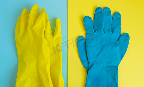 双桌背景平铺黄色和蓝色橡胶防护手套，用于春季或日常清洁。
